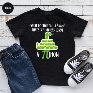 May include: A black short-sleeve t-shirt featuring a green snake graphic coiled in a spiral with the pi symbol on its body. The text reads: What do you call a snake that's 3.14 meters long? A pi-thon, with the pi symbol replacing the letter p.