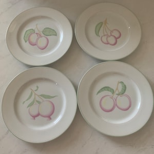 May include: Set of four white ceramic dinner plates with a green rim. Each plate features a different fruit design: cherries, plums, and peaches.