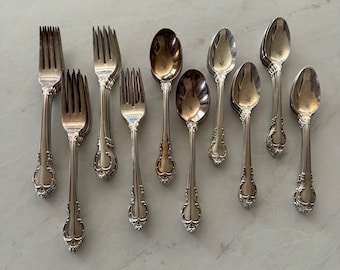 May include: A set of silverware, including forks and spoons, with ornate handles. The silverware is made of polished silver and has a classic design.
