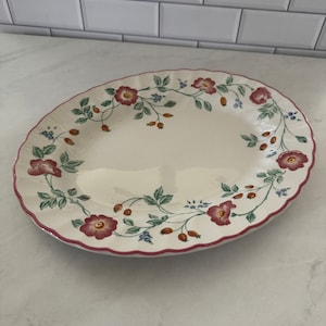 May include: A white oval serving platter with a pink, red, and green floral design. The platter has a scalloped edge.