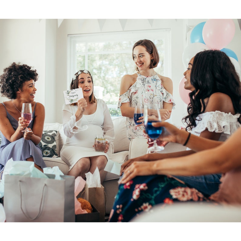 May include: Four women are gathered together, one of whom is pregnant and holding a card that says "Congrats on Baby Girl". The women are smiling and laughing, and there are blue and pink balloons in the background.