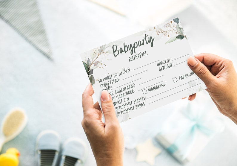 May include: A white card with a floral design and the text "Babyparty Ratespiel" printed on it. The card has a list of questions to guess about a baby, such as the baby's name, birthdate, eye color, hair color, and gender.