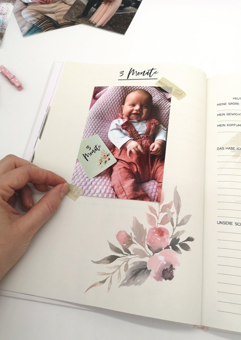 May include: A baby girl wearing a red overall and white shirt is lying on a pink blanket. The photo is in a scrapbook with a handwritten note that says "3 Monate" which is German for "3 months".