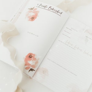May include: A pink and white baby journal with the text "4 Monate Babygl&uuml;ck" on the cover. The journal has a watercolor floral design and is open to a page with the text "HEUTE IST DER" and "MEINE GROSE".