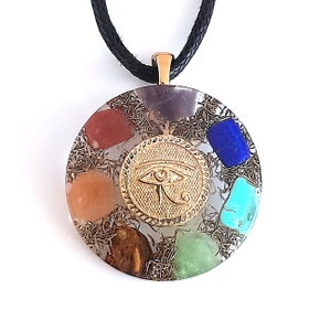 May include: A round, clear crystal pendant with a gold Eye of Horus charm in the center. The pendant is surrounded by seven smaller crystals in various colors, including red, orange, yellow, green, blue, and purple. The pendant is attached to a black cord.