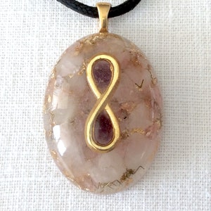 May include: A gold infinity symbol pendant with a pink and white crystal stone. The pendant is on a black cord.