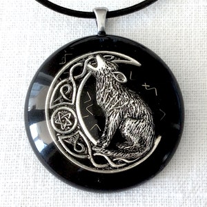 Puede incluir: Un collar con un colgante negro que representa un lobo plateado aullando a la luna. El colgante está rodeado por un diseño de nudo celta.