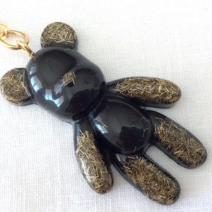 May include: Black resin teddy bear keychain with gold glitter accents. The bear is attached to a gold chain.