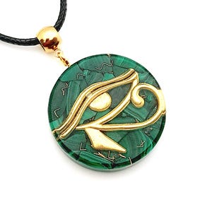 May include: A round green malachite pendant with a gold Eye of Horus design. The pendant is on a black cord.