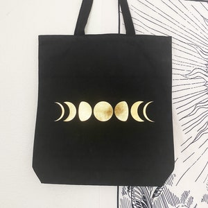 May include: Black canvas tote bag with gold moon phases printed on the front.