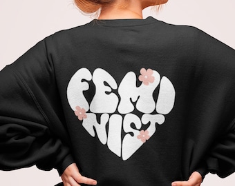 May include: Black sweatshirt with a white heart-shaped graphic that says "FEMINIST" in a retro font. The heart has three small pink flowers.