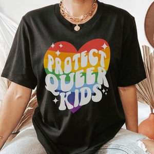 Puede incluir: Camiseta negra con un gr&aacute;fico de coraz&oacute;n arco&iacute;ris que dice "Proteger a los ni&ntilde;os queer".