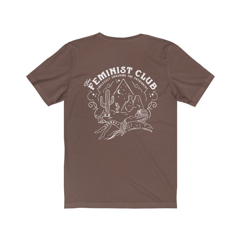 May include: A brown t-shirt with a white graphic design. The graphic features a desert scene with a cactus, mountains, and a crescent moon. The text "The Feminist Club" is written in a circular design around the scene. The text "Tirelessly Smashing the Patriarchy" is written in a smaller font below the scene. The text "Once Literally Forever" is written in a smaller font below the scene.