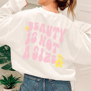 May include: White sweatshirt with a pink graphic that says "Beauty is not a size" with yellow flowers on the back.