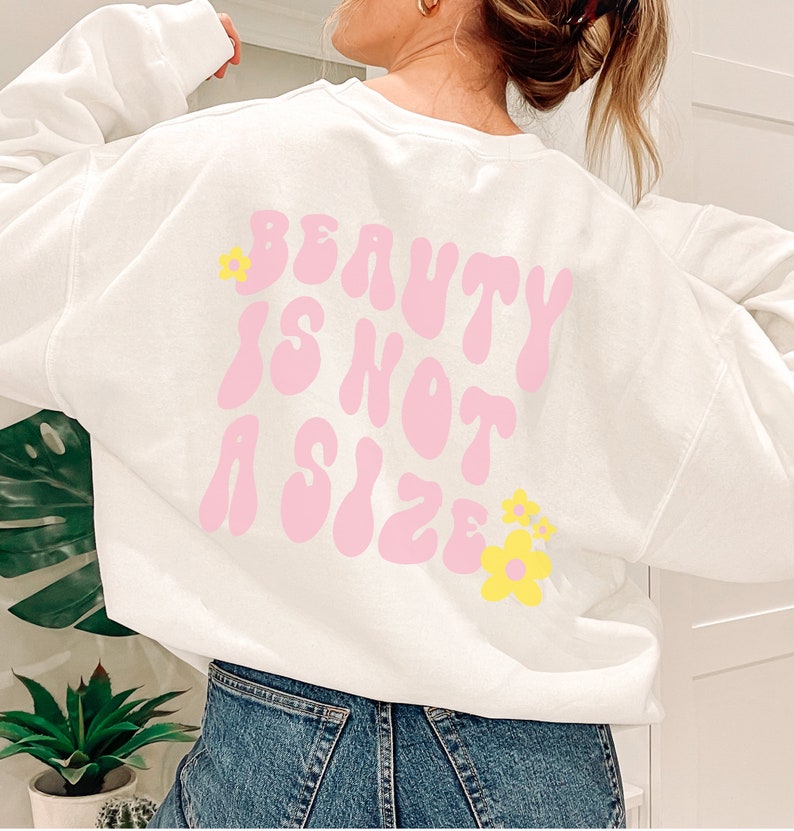 May include: White sweatshirt with a pink graphic that says "Beauty is not a size" with yellow flowers on the back.