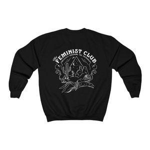 Może przedstawiać: Czarna bluza z białym nadrukiem przedstawiającym scenę z pustyni z tekstem "The Feminist Club Tirelessly Smashing The Patriarchy Since Literally Forever"
