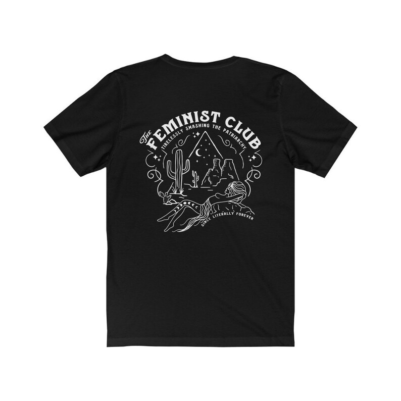 May include: Black t-shirt featuring a white graphic design of a desert scene with a cactus, mountains, and a crescent moon. The text "The Feminist Club" is in a circular design around the scene. The text "Tirelessly Smashing the Patriarchy" is in a smaller font above the scene. The text "Once Literally Forever" is in a smaller font below the scene.