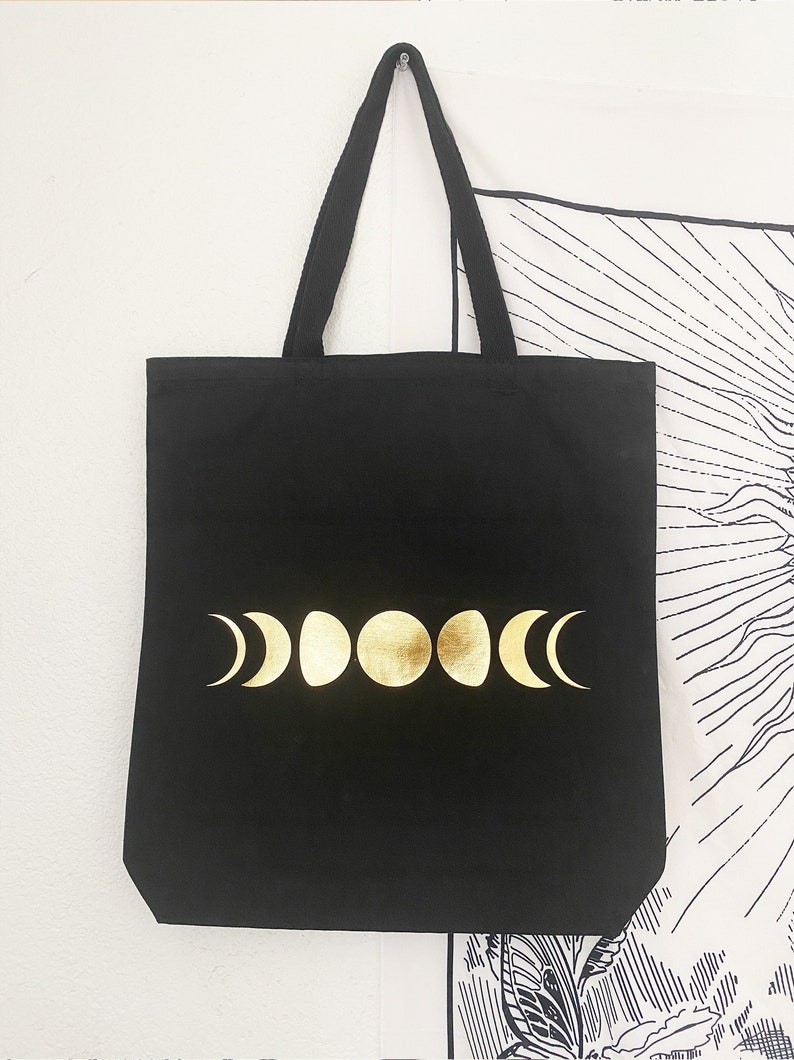 May include: Black canvas tote bag with gold moon phases printed on the front.