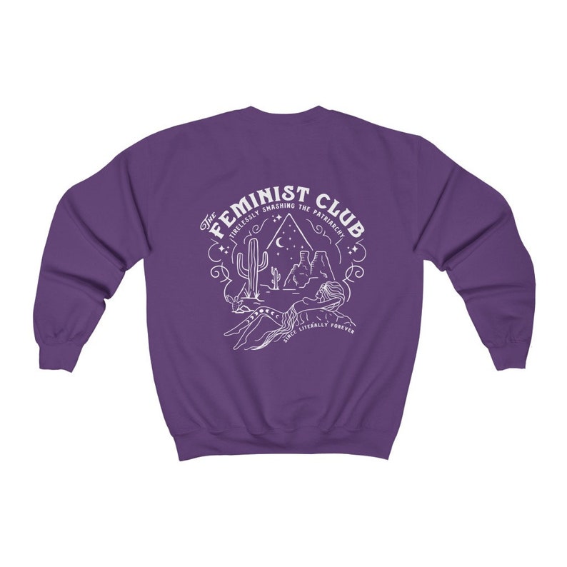 Może przedstawiać: Fioletowa bluza z białym nadrukiem graficznym, na kt&oacute;rym widnieje napis "The Feminist Club" wraz ze sceną pustynną i tekstem "Tirelessly Smashing the Patriarchy Since Literally Forever".