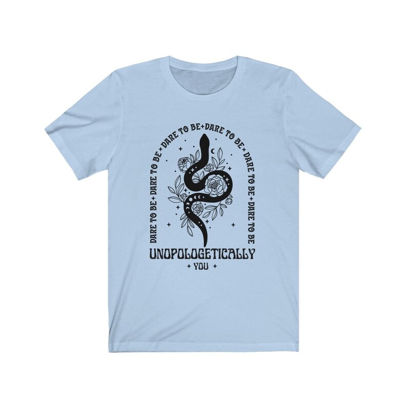 Pu&ograve; includere: Maglietta blu chiaro con un serpente nero e un disegno floreale. Il testo "DARE TO BE+DARE TO BE DARE TO BE+DARE TO BE TO BE DARE TO BE UNOPOLOGETICALLY + YOU +" &egrave; stampato sulla maglietta.