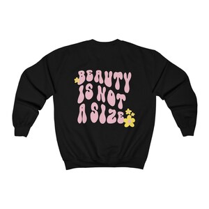 May include: Black sweatshirt with the text "BEAUTY IS NOT A SIZE" in pink with yellow flowers.