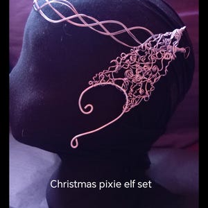 May include: A light pink wire headband and ear cuff set. The headband has a wavy design, and the ear cuff features intricate swirls and loops. The text "Christmas pixie elf set" is visible at the bottom of the image.