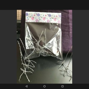 May include: A clear plastic bag containing silver wire art, with more pieces scattered around. The bag is sealed with a floral patterned top. The wire art appears to be small, abstract sculptures.