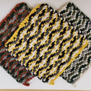 Puede incluir: Tres agarraderas de olla tejidas en diferentes patrones de colores. La primera es un patr&oacute;n marr&oacute;n, verde y gris. La segunda es un patr&oacute;n amarillo, negro, blanco y gris. La tercera es un patr&oacute;n verde, gris y blanco.