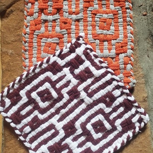 May include: Two woven pot holders, one with a white and orange geometric pattern and the other with a white and brown geometric pattern.