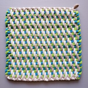 Puede incluir: Un agarrador de olla tejido con un patr&oacute;n diagonal en tonos de verde, azul, blanco y marr&oacute;n.