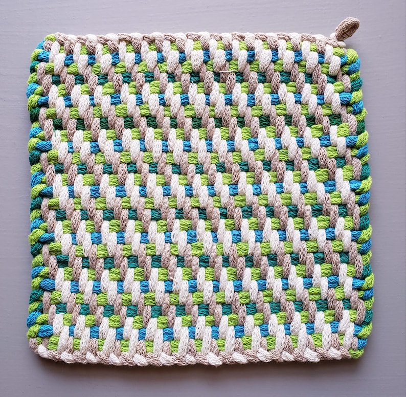 Puede incluir: Un agarrador de olla tejido con un patr&oacute;n diagonal en tonos de verde, azul, blanco y marr&oacute;n.