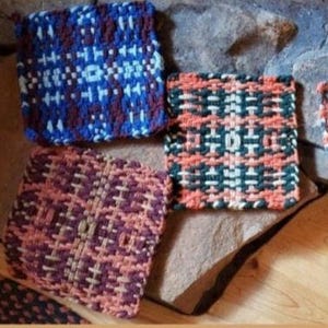 May include: Four woven pot holders in different patterns and colours. The pot holders are made with a variety of yarns in shades of blue, green, brown, orange, and white.