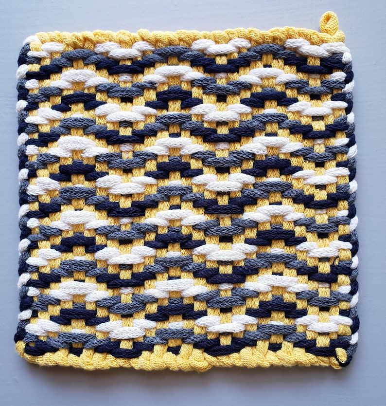 Puede incluir: Un posavasos tejido amarillo, blanco, gris y negro con un borde de flecos.