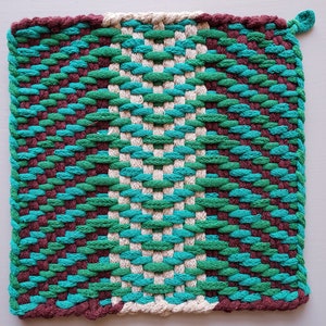 Puede incluir: Un posavasos tejido con un patr&oacute;n geom&eacute;trico en tonos marrones, verdes y azules.