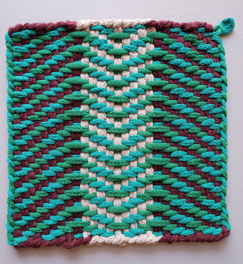Puede incluir: Un posavasos tejido con un patr&oacute;n geom&eacute;trico en tonos marrones, verdes y azules.