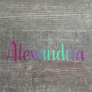 May include: The name Alexandria is spelled out in colorful letters on a woodgrain background. The letters are pink, purple, blue, and green.