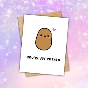 May include: A white greeting card with a brown potato illustration and the text "YOU'RE MY POTATO" in black. The potato has a cute face with pink cheeks and a small pink heart above it. The card is on a brown backing.
