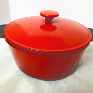 Op de afbeelding: Een felrode gietijzeren braadpan met een bijpassende deksel en een kleine, ronde handgreep. De pot heeft aan weerszijden twee donkergrijze handvatten. Dit kookgerei is ideaal voor slow cooking en bakken.