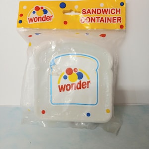 May include: A clear plastic sandwich container shaped like a slice of bread. The container is in a clear plastic bag with a yellow header that reads "SANDWICH CONTAINER" and the "wonder" logo.