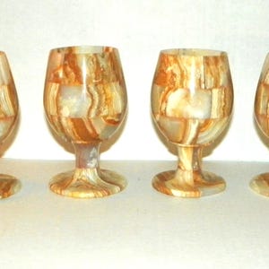 Pode incluir: Quatro taças de vinho decorativas com um padrão de mosaico de pedra bege, castanho e creme. Cada taça tem uma taça arredondada, uma haste fina e uma base circular. As taças estão dispostas em fila.