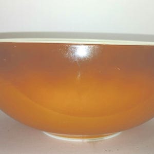 Könnte beinhalten: Eine große, vintage Rührschüssel mit einem Farbverlauf, der von einem tiefen Braun oben zu einem warmen Orange an der Basis übergeht. Die Schüssel hat einen weißen Rand und zwei Griffe.