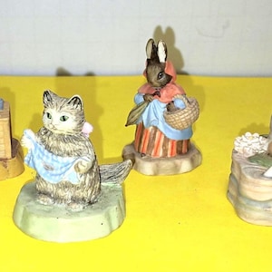 May include: A collection of six miniature animal figurines including a duck in a bonnet, a mouse, a cat holding a blue cloth, a rabbit in a red shawl, a frog sitting on a rock, and a rabbit crawling through a wooden fence structure.