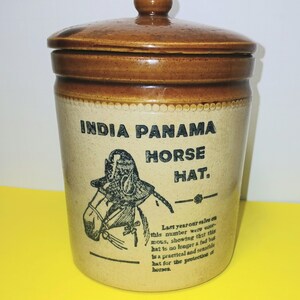 May include: A vintage ceramic jar with a lid. The jar is tan with brown accents and features the text "INDIA PANAMA HORSE HAT." A graphic of a horse wearing a hat is also present, along with additional text.