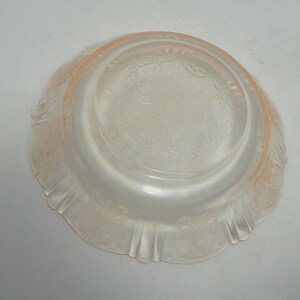 May include: A pale pink translucent glass bowl featuring a circular base and a wide, flared rim. The exterior surface is decorated with a repeating embossed floral pattern and vertical fluting along the edges, creating a textured appearance.