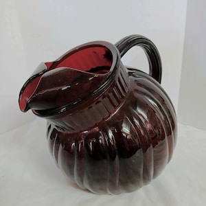 May include: A white ceramic mug with a black handle and the text "But First, Coffee" in a black, bold font. The mug is sitting on a white surface. The mug is approximately 4 inches tall.