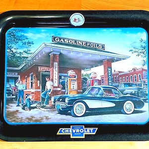 May include: A rectangular black serving tray featuring a vintage petrol station scene with a classic Chevrolet sports car, a brick building labelled Gasoline Oils, and a Chevrolet logo at the bottom centre with a small circular emblem at the top.