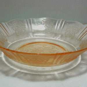 May include: A shallow, round, peach-colored glass bowl featuring a scalloped rim and a textured, embossed floral pattern around the interior sides and a detailed, intricate geometric design centered on the bottom of the basin.