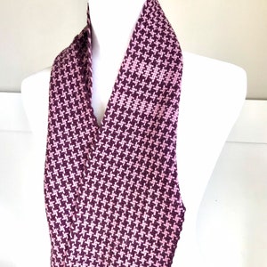 May include: A pink and burgundy woven scarf with a houndstooth pattern and a fringe trim.