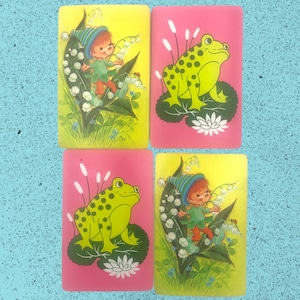 May include: Four colorful cards with illustrations of a green frog and a fairy-like character. The cards are pink, yellow, and blue with green leaves and white flowers.