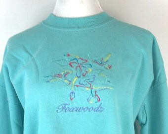 May include: A turquoise blue sweatshirt with an embroidered design of colorful flowers and the word "Foxwoods" in purple.